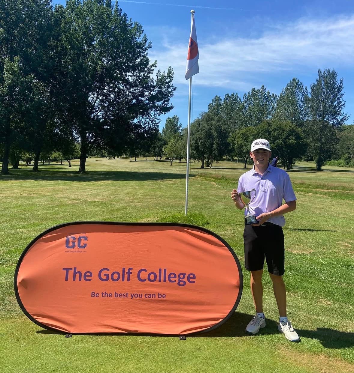Sam Eynon holding a trophy beside a The Golf College banner